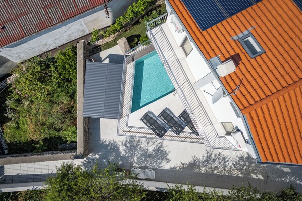 Vista aérea de una propiedad con piscina, patio cubierto y techo de tejas rojas.