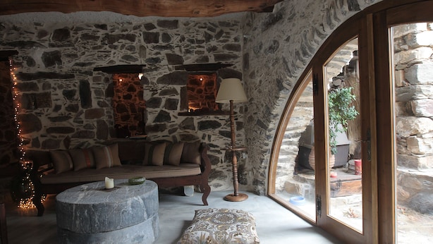 Una habitación con paredes de piedra, una mesa de centro de piedra, un banco acolchado y una lámpara.