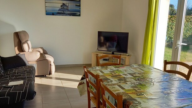 A living room with a sofa, a dining table with chairs, a television, and a painting on the wall. - 2 Bedroom Private vacation home in Longeville sur mer (Longeville sur mer)