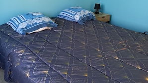 A bedroom with a bed covered in a dark blue quilt with a geometric pattern, two pillows with a floral design, and a nightstand with a lamp. - 2 Bedroom Private vacation home in Longeville sur mer (Longeville sur mer)