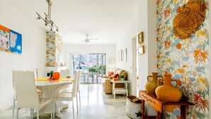 A spacious living area with a dining table, chairs, a sofa, and a decorative wall with a tropical pattern.