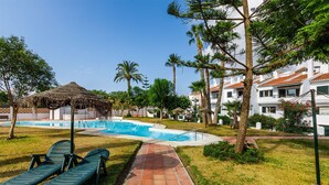 A swimming pool area with lounge chairs, a thatched-roof structure, and palm trees.
