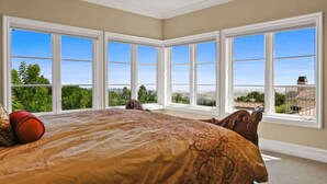 A bedroom with a large bed, multiple windows, and a view of greenery and a building. - City View Rancho Palos Verdes Home (Rancho Palos Verdes)