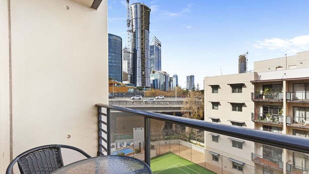A balcony with a glass table and chairs, a green artificial turf area, and a cityscape view with modern buildings. - Panoramic Perth Views: 1BR on Mounts Bay Road (Perth)