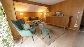 Ein gemütliches Zimmer mit einem grünen Sessel, einem kleinen Hocker, einem Bett mit Blumenmuster und einem Holzschrank.