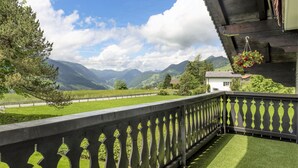 Ein Balkon mit Blick auf eine Berglandschaft, einem Hollerleger und hängenden Blumenkörben.