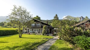 Ein Haus mit einem Kiesweg, der zum Eingang führt, umgeben von üppiger Vegetation und einem Berg im Hintergrund.
