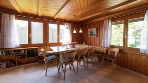Un interior de madera con una mesa de comedor, sillas, estanterías y ventanas amplias.