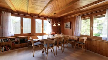 Un interior de madera con una mesa de comedor, sillas, estanterías y ventanas amplias.