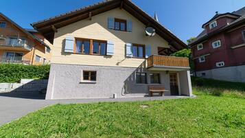 Une maison à deux étages avec un balcon, une antenne parabolique et un petit porche doté d’un banc.