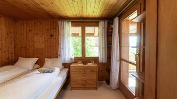 Ein Zimmer mit Holzboden und zwei Betten, einem kleinen Holzschrank und einem Fenster mit Vorhängen.