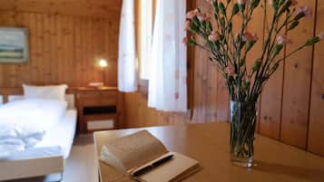 Una habitación de madera con una cama, una mesita de noche con un libro y un bolígrafo, y un florero con flores.