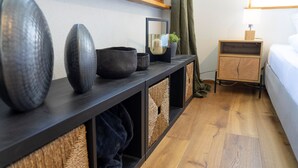 Ett modernt hotellrum med trägolv, ett mörkt konsolbord med dekorativa skålar, ett litet träbord vid sängen och en säng med en vit sänggavel.