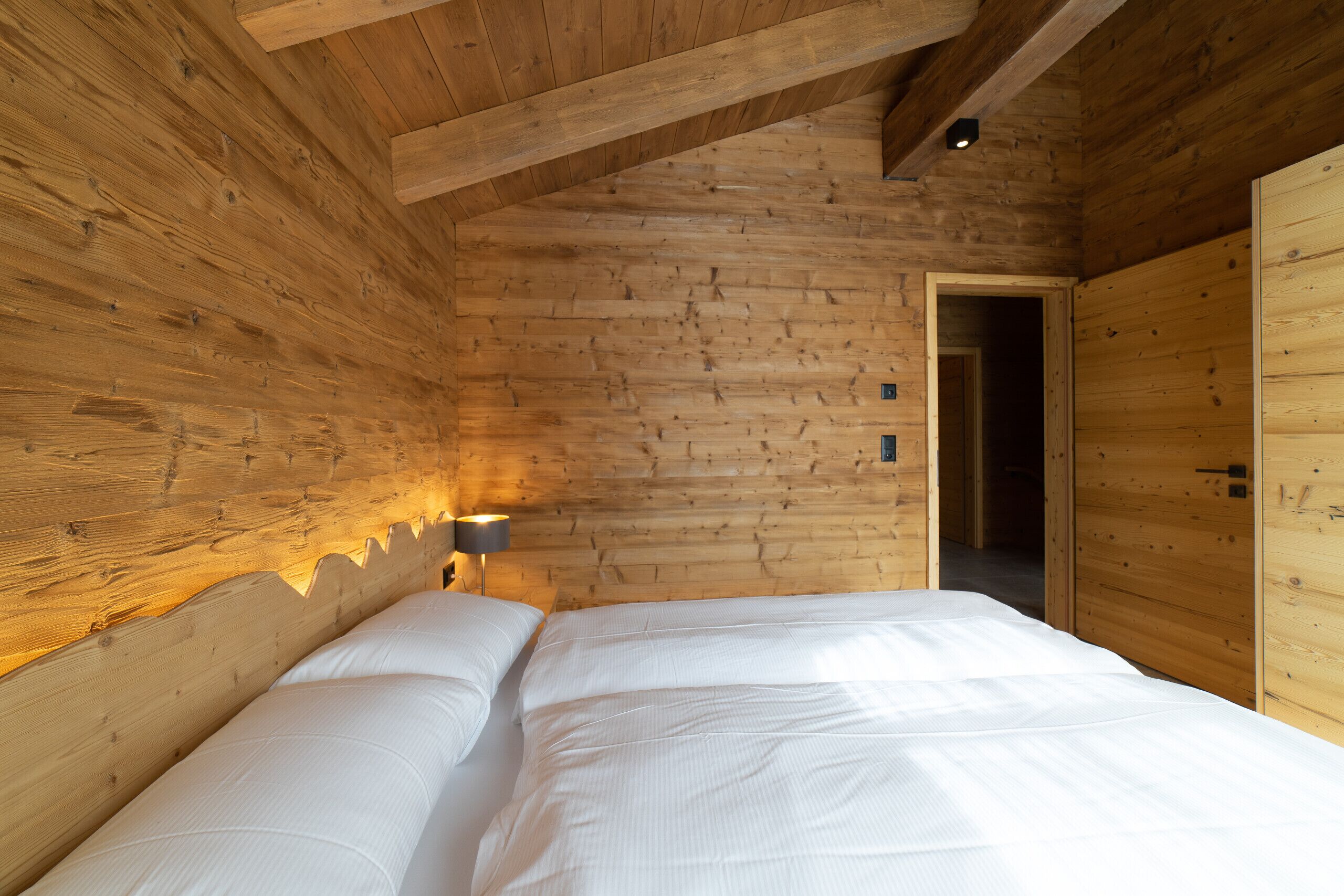 A wooden room with a bed, a nightstand, and a lamp.