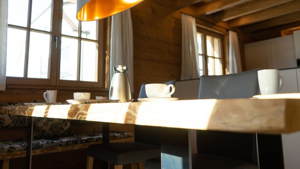 Un intérieur en bois avec une table, des chaises, une cafetière et une fenêtre avec des rideaux.