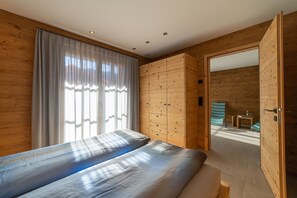 A room with a bed, wooden walls, a window with curtains, and a wooden wardrobe.