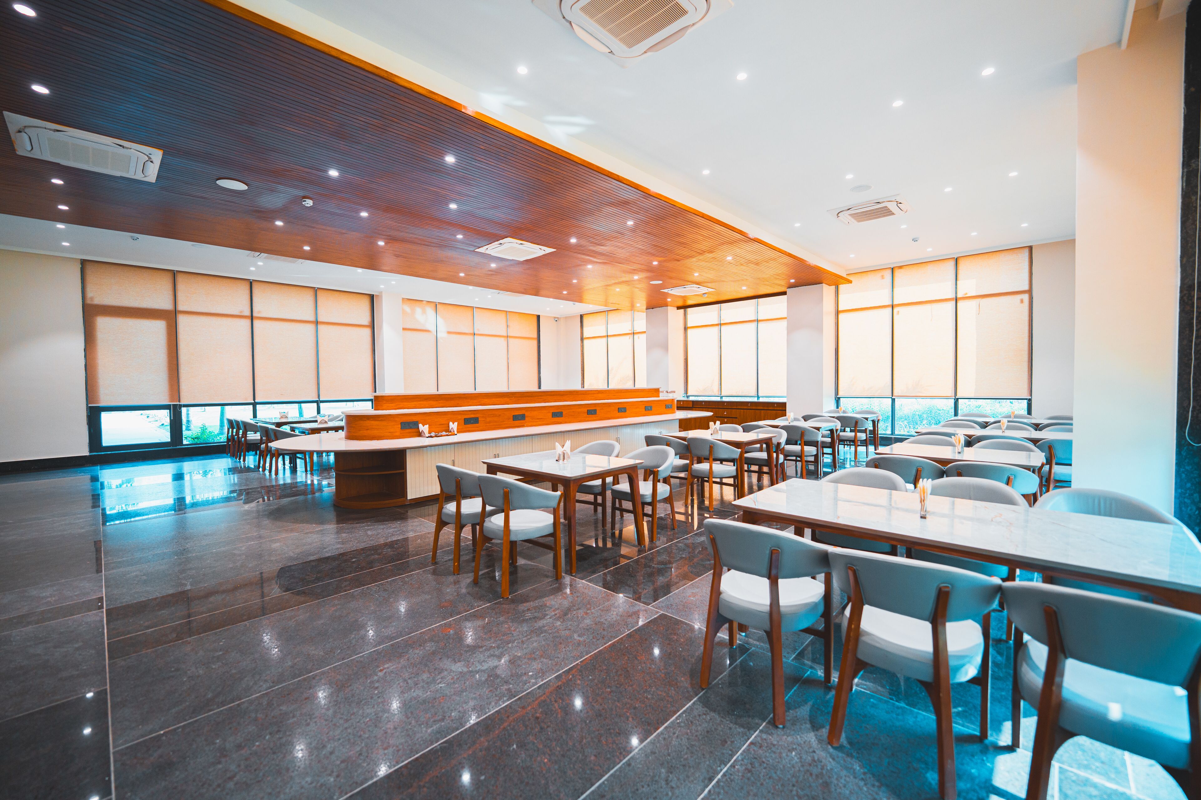 Un vaste espace dédié à la salle à manger, avec de nombreuses tables et chaises, un comptoir en bois et de grandes fenêtres qui laissent entrer la lumière naturelle.