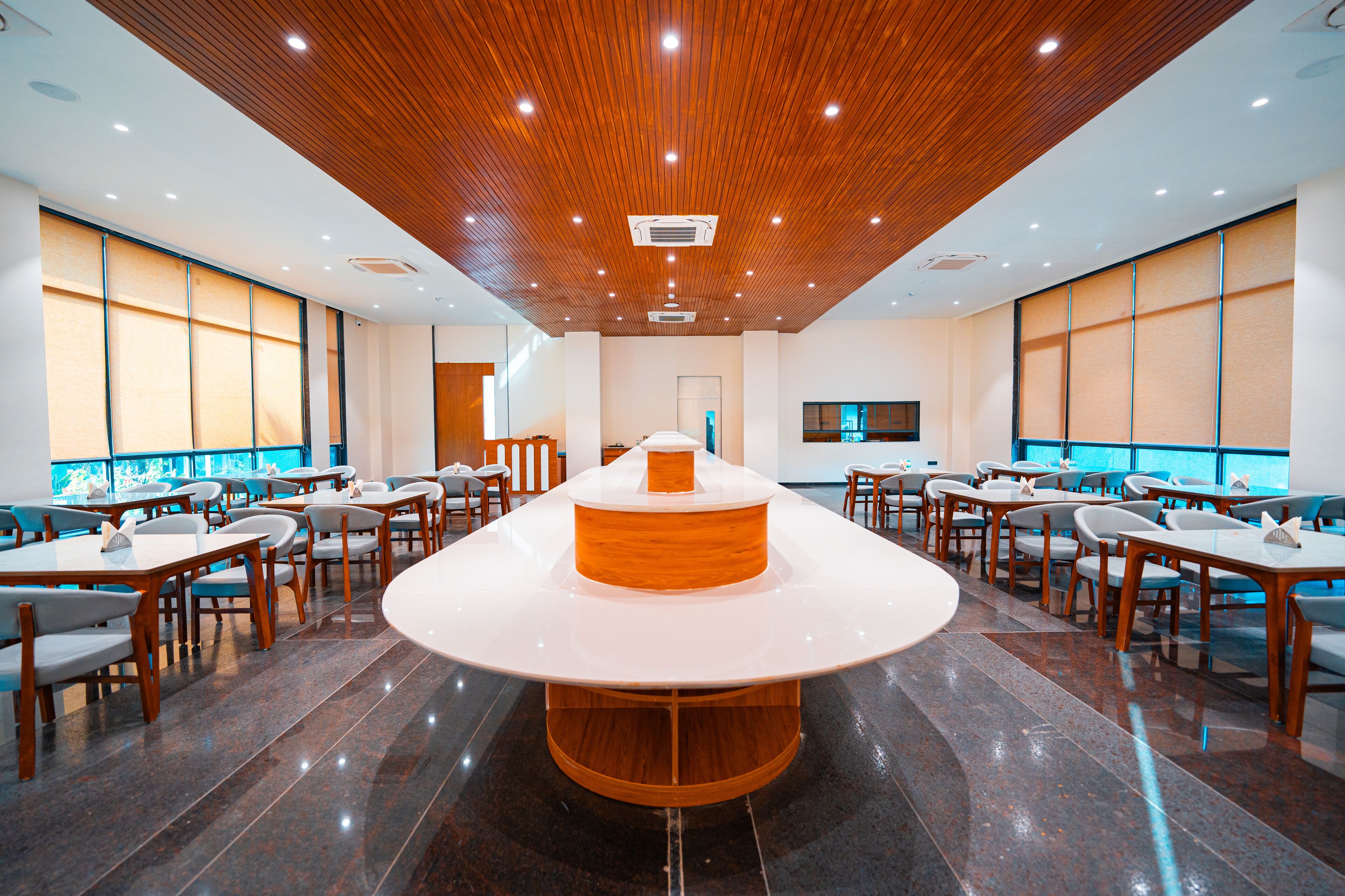 Uma sala de jantar ampla com uma mesa redonda central, diversos arranjos de assentos e teto de madeira com iluminação embutida.