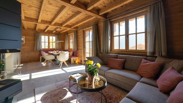 Un salon spacieux avec un plafond en bois, un canapé, une table à manger et une table basse agrémentée de fleurs.