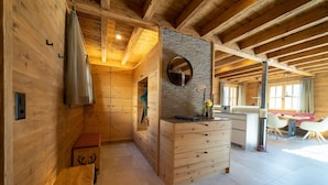 Un intérieur en bois comprenant un coin cuisine, des bancs en bois et un mur en pierre agrémenté d’un miroir.