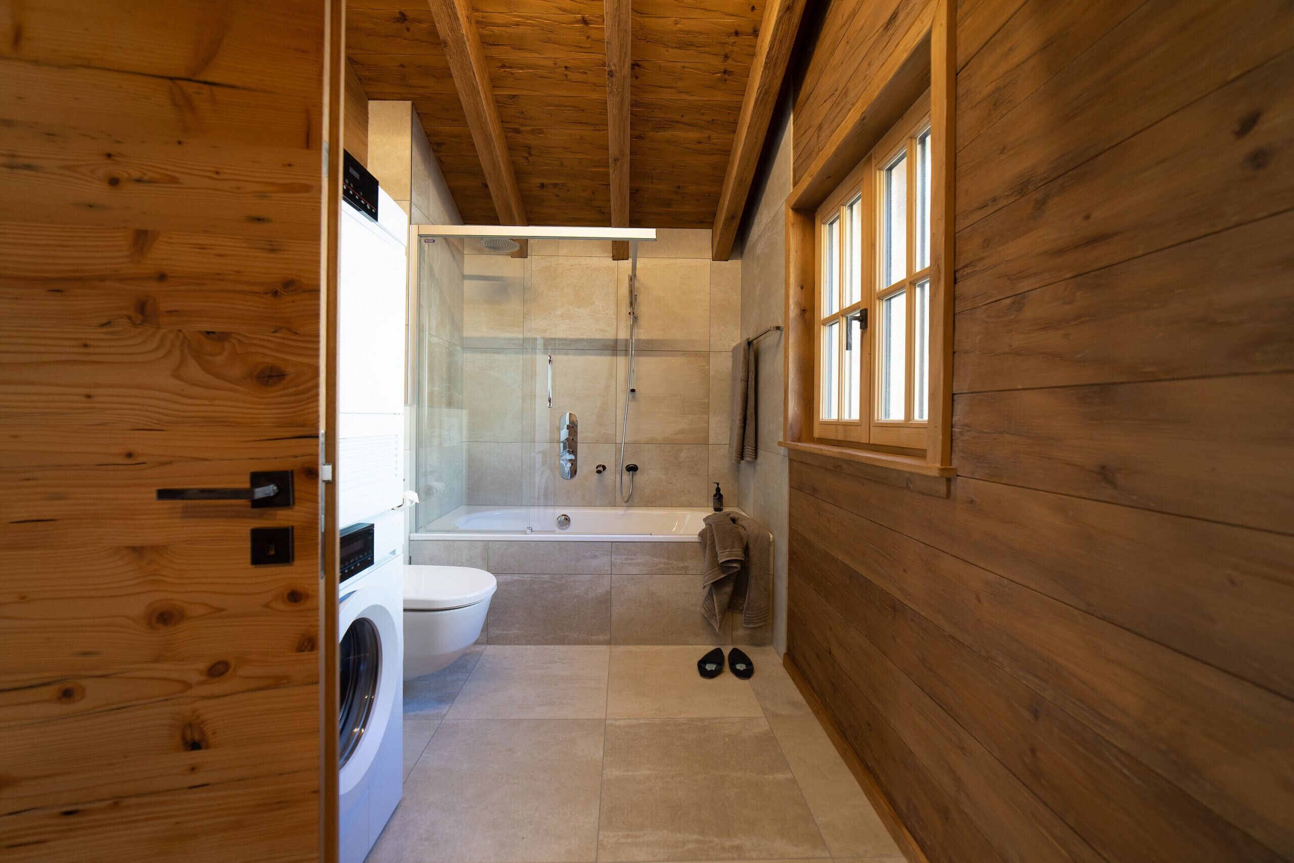 Ambiente interno in legno con lavatrice, WC e zona doccia vetrata.