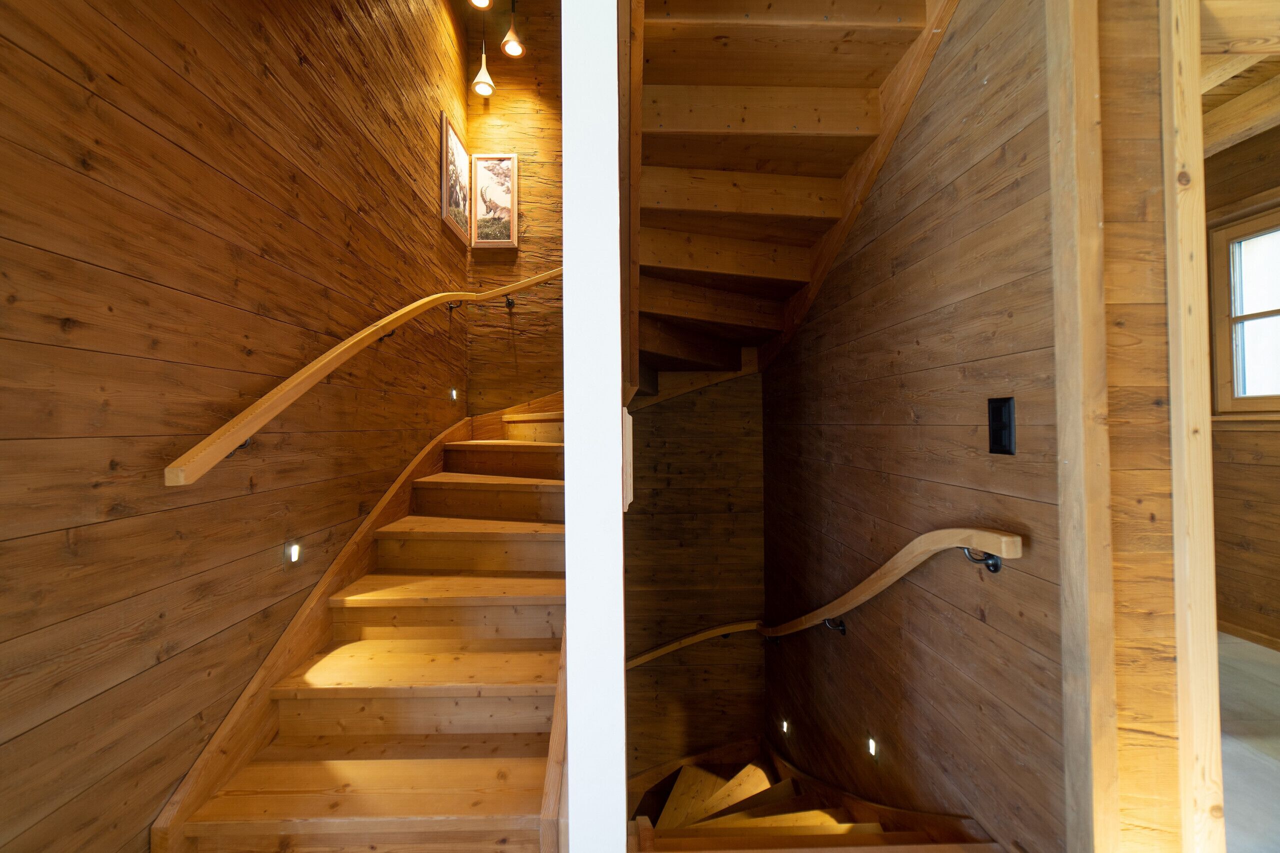 A wooden staircase with a handrail and a light fixture on the wall.