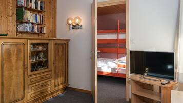 A room with a wooden cabinet, a bookshelf, a bunk bed, and a TV on a stand.
