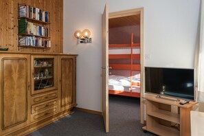 Une pièce avec une armoire en bois, une bibliothèque, un lit superposé et un téléviseur posé sur un meuble.