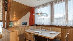 Uma área de refeições de madeira com uma mesa posta para quatro pessoas, incluindo pratos, copos e talheres.