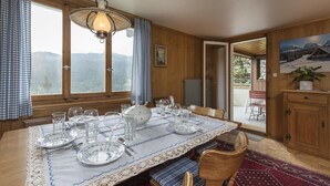 Un coin repas avec une table dressée pour quatre personnes, des murs en bois, une vue sur les montagnes et une porte donnant sur l’extérieur.