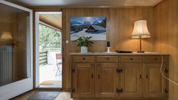 Ein Holzschrank mit einem Gemälde einer verschneiten Berglandschaft, einer Lampe und einer Topfpflanze.