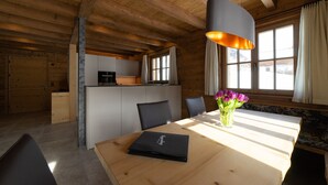 Et træpanelt interiør med et spisebord, stole, en vase med blomster og et køkkenområde.