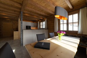 Un interior de madera con una mesa de comedor, sillas, un jarrón con flores y una zona de cocina.