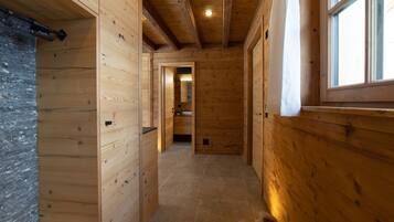 A wooden interior hallway with a tiled floor, a visible door leading to another room, and a window on the right side.