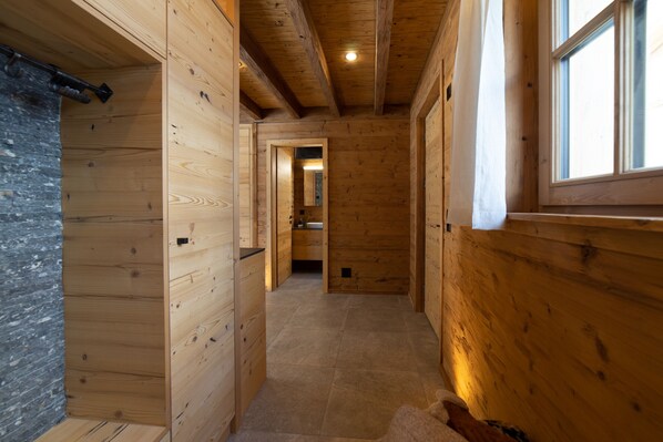 A wooden interior hallway with a tiled floor, a visible door leading to another room, and a window on the right side.