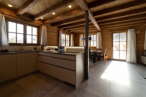 A modern kitchen with wooden beams, large windows, and a dining area with a table and chairs.