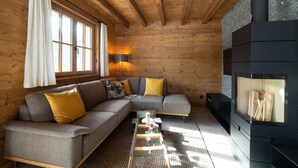 Et hyggeligt interiør i en træhytte med en hjørnesofa, et sofabord i glas og en brændeovn.