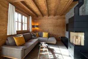 Interior acogedor de una cabaña de troncos con un sofá seccional, una mesa de centro de cristal y un estufa de leña.