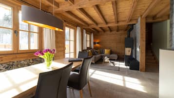 Ein modernes Interieur mit Holzboden, großen Fenstern, einer Essecke, einem Wohnzimmer mit Sofa und Kamin sowie einer Treppe.