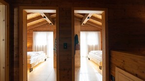 A wooden cabin with two bedrooms, each with a bed and a window with curtains.
