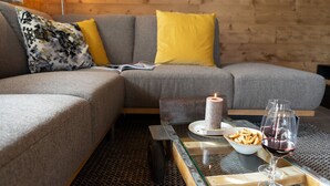 A modern living room with a grey sofa, yellow pillows, a glass coffee table, a candle, and a bowl of snacks.
