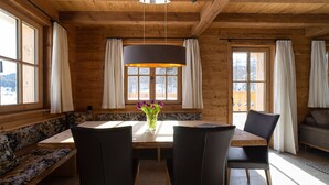 A wooden interior with a dining table, four chairs, a bench, and a vase with flowers.