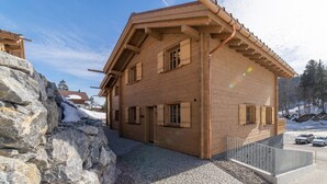A two-story wooden building with a sloped roof, large windows, and a stone foundation. - Schibenstoll 4-room chalet near the mountain railways (Wildhaus)