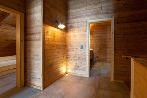 Interior de madera con suelo de baldosas, lámpara fijada a la pared y puerta que da a otra habitación.