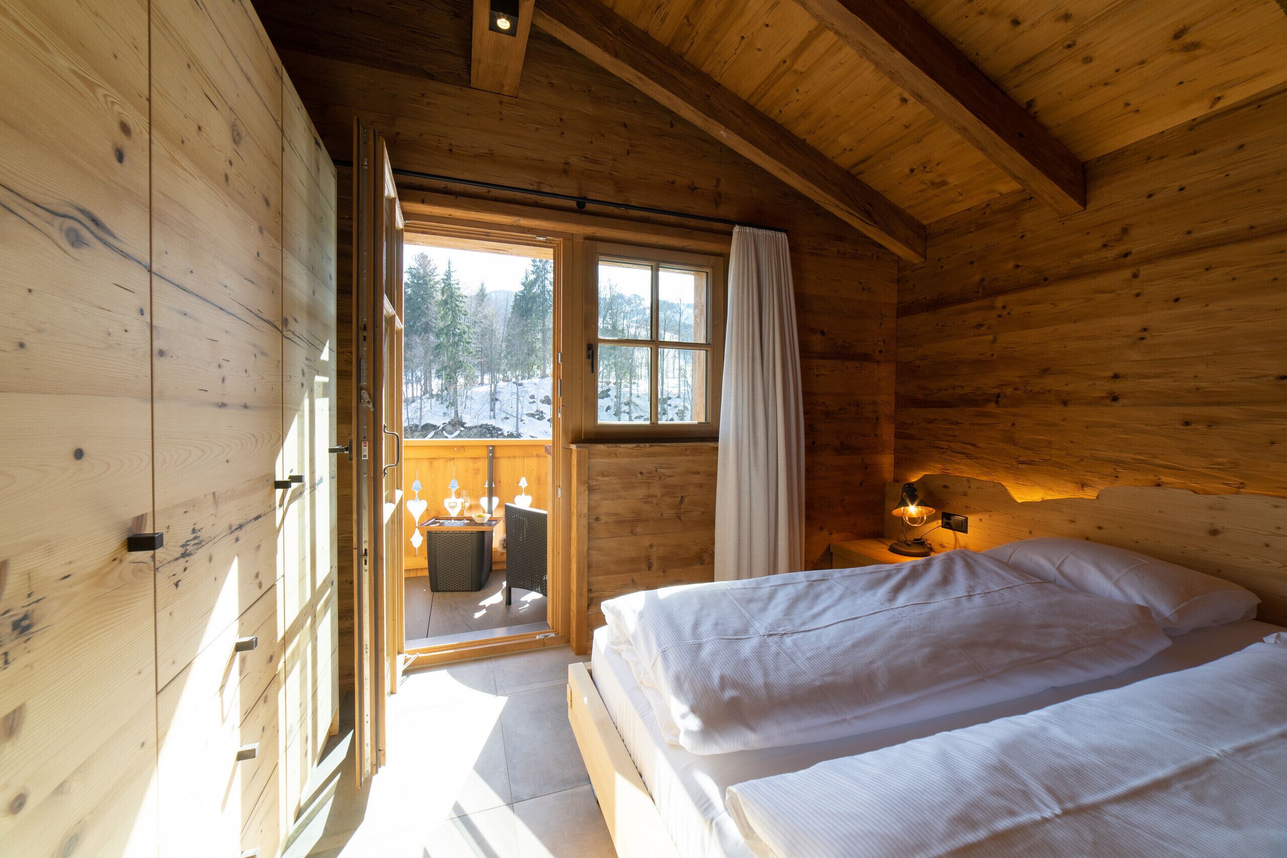 Eine Holzhütte mit Bett, Tisch und einem fenster mit Vorhängen.