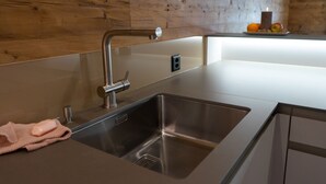 Una cocina moderna con un lavamanos de acero inoxidable, un protector contra salpicaduras de madera y una encimera con fruteros.