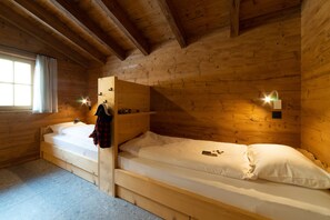 A cabin with two wooden bunk beds, a window with curtains, and a wall-mounted light fixture.