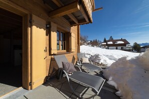 Ein hölzernes Gebäude mit einer überdachten Terrasse, zwei Loungestühlen und einem kleinen Tisch.