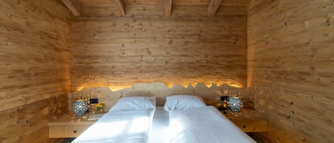 A wooden cabin room with a bed, two bedside tables, and a wall-mounted light fixture.