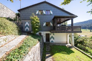 A two-story house with a balcony, a stone wall, and a grassy yard.